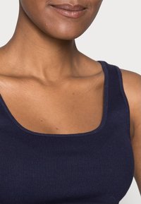 Marinblå ribbad linne med fyrkantig urringning och breda band. Mjuk textur med en figurnära design, passande för vardagsbruk.