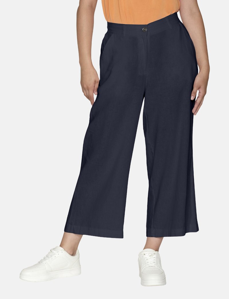Marina vida byxor med hög midja, med framfickor och en enda knappstängning, i kombination med vita sneakers.