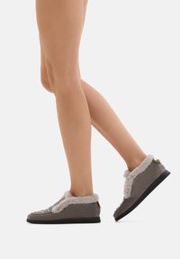 Scarpe morbide grigie con foderatura in pelliccia e accenti decorativi, dotate di punta arrotondata e tomaia testurizzata. Suola nera e dettagli in oro discreti.