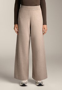 Breda byxor i en ljusbeige tyg med en mjuk textur, med ett ribbat högt midjeband och sid sömmar. Kombinerat med vita sneakers.
