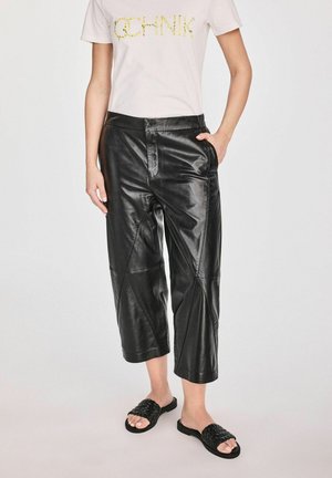 Czarne skórzane spodnie w kroju cropped o gładkiej fakturze i ukośnych szwach. W zestawie z białym t-shirtem i czarnymi plecionymi klapkami.