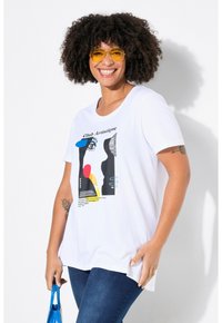Camiseta blanca de manga corta con un estampado gráfico de formas abstractas y texto. El modelo sostiene un bolso azul y lleva puestas gafas de sol amarillas.