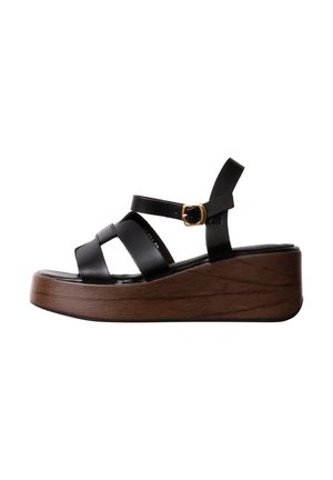 Sandale plateforme en cuir noir avec semelle compensée en bois et bride de cheville avec boucle dorée, vue latérale sur fond blanc.