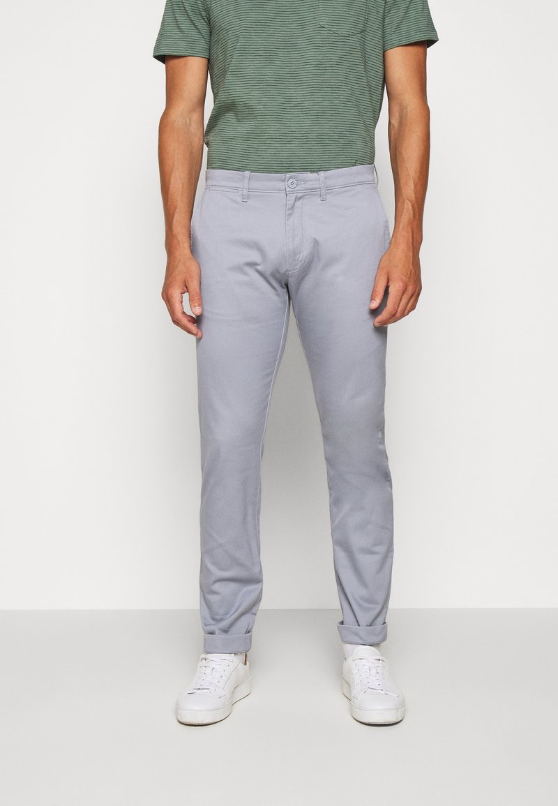 Pantaloni grigio chiaro a vestibilità slim, orli risvoltati, tasche frontali e chiusura con un solo bottone, abbinati a una t-shirt verde a righe.