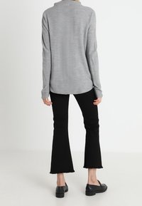 Graues Langarmoberteil mit strukturierter Oberfläche, kombiniert mit schwarzen Flared-Jeans und schwarzen Slippern, mit einem lässigen Schnitt und abgerundetem Saum.