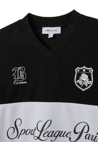 Camiseta deportiva en blanco y negro con diseño en forma de V. Presenta una tela texturizada, un logo bordado y el texto "Sport League Paris" en cursiva.