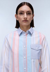 Camicia a righe button-up in colori pastello, con linee verticali e una tasca sul petto con un bordo a righe blu e bianche. Tessuto di cotone.
