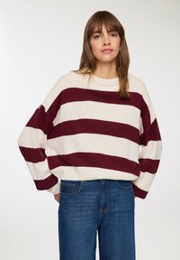 Sweter w burgundowe i kremowe paski, z opadającymi ramionami, okrągłym dekoltem i prążkowanymi mankietami, zestawiony z niebieskimi dżinsami o wysokim stanie.