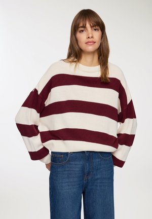 Maglione a righe bordeaux e crema con spalle scese, colletto rotondo e polsini a costine, abbinato a jeans blu a vita alta.