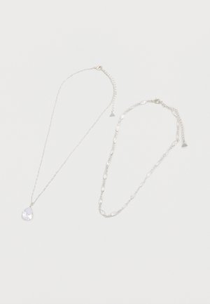 Două coliere de argint pe un fundal alb, unul cu un pandantiv de cristal în formă de picătură, celălalt cu zale ovale de cristal.