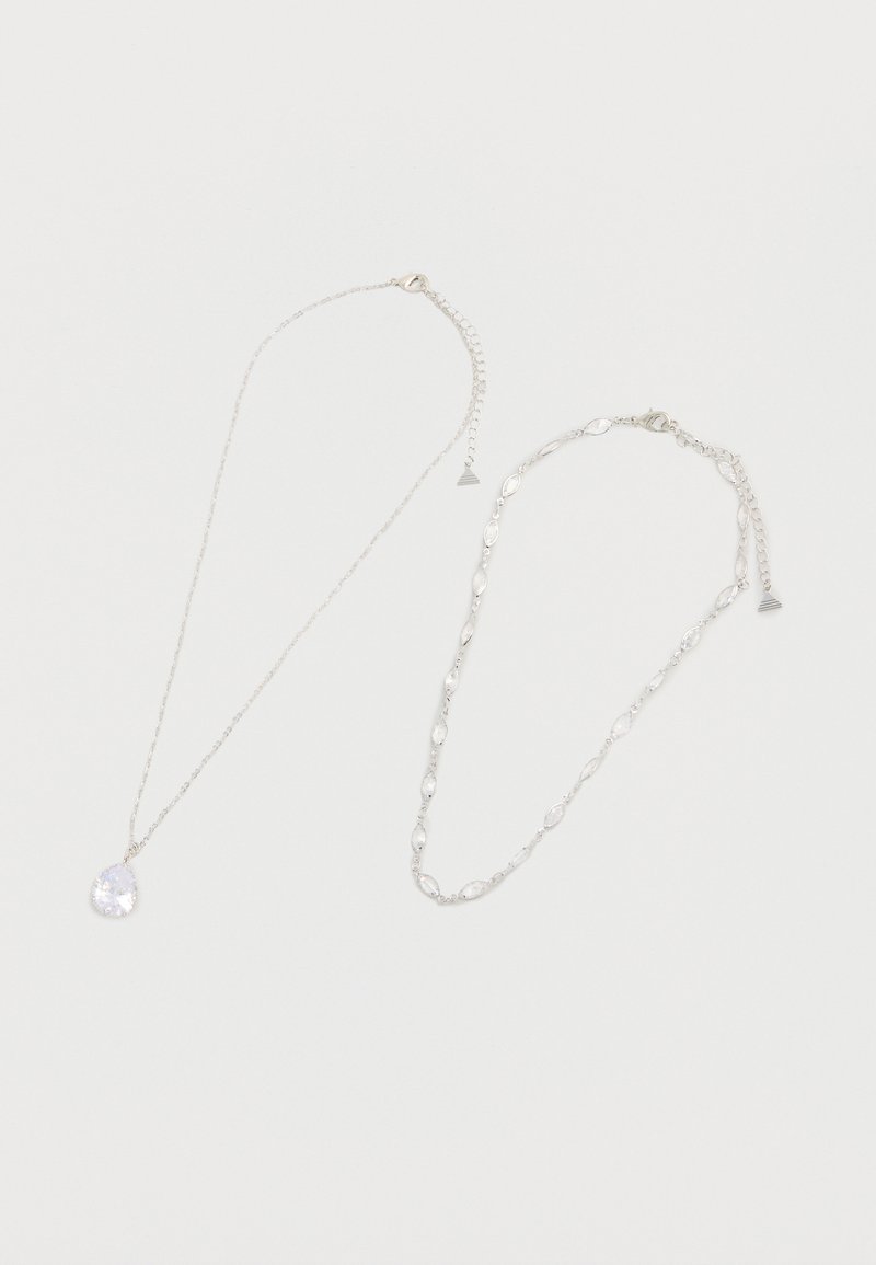 Deux colliers en argent sur fond blanc, l'un avec un pendentif en cristal en forme de goutte, l'autre avec des maillons ovales en cristal.