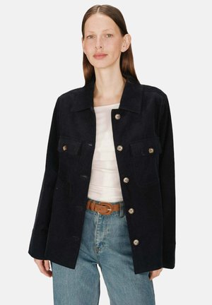 Veste en velours côtelé marine avec un col, des boutons de fermeture et deux poches avant, associée à un jean bleu clair et un haut blanc.