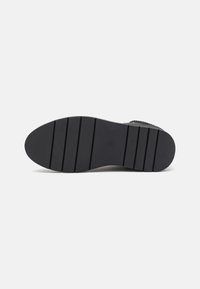 Black shoe sole featuring a textured rubber surface with horizontal grooves for traction and a smooth, rounded toe design.