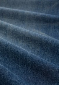 Denimstoff in einem mittleren Blauton mit einer glatten Textur, der subtile Farbvariationen und ein klassisches Webmuster aufweist.