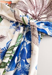 Tissu torsadé en nœud avec des imprimés botaniques bleus, verts et bruns sur un fond beige et blanc.