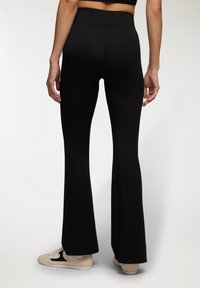 Czarne legginsy dzwony wykonane z elastycznego materiału, z wysokim pasem i gładką teksturą. Noszone z jasnym obuwiem sportowym.