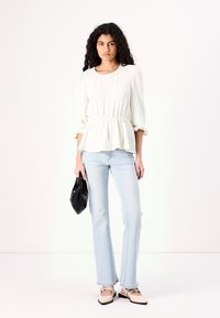 Haut peplum blanc à côtes avec des manches longues, associé à un jean évasé bleu clair. Sac à main noir et chaussures bicolores beiges.