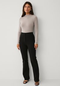 Langärmliges, hellgraues Oberteil, kombiniert mit hochtaillierten, schwarzen Schlaghosen. Enger Schnitt, glatte Textur. Einfache Sandalen runden das Outfit ab.