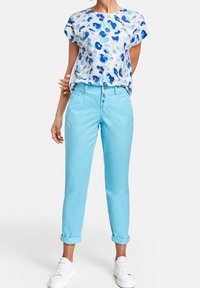 Kortärmad blå och vit mönstrad blus som matchas med ljusblå byxor med uppvikta ärmar och vita sneakers. Mjuk tyg, avslappnad passform, avslappnad stil.