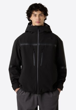 Giacca softshell nera con cappuccio, dotata di tasche sul petto con zip, strisce a contrasto e finitura opaca. Chiusura con zip frontale.