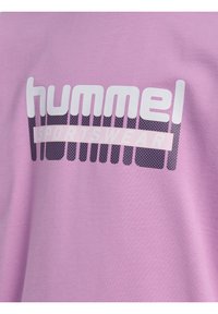 Maglietta corta rosa con maniche a breve che presenta un grande logo "hummel" bianco e viola e il testo "SPORTSWEAR", con una morbida consistenza di cotone.