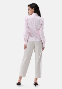 Hellrosa gestreiftes Hemd mit langen Ärmeln, Manschetten mit Knöpfen und einem taillierten Rücken, kombiniert mit beigen weiten Hosen und Sandalen mit Absatz.