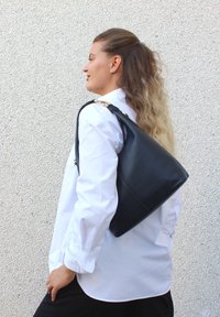 Svart läderhandväska med texturerad yta och triangulär form, med ett handtag ovanpå och detaljer i guldton.