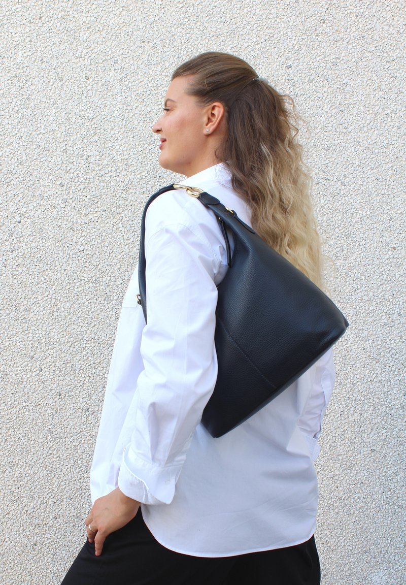 Svart läderhandväska med texturerad yta och triangulär form, med ett handtag ovanpå och detaljer i guldton.