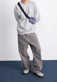 Grå sweatshirt med vita ränder, grå kordflöjlsbyxor och grå skor, kompletterat med en liten crossbody-väska med lila accenter.