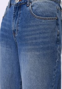 Jeans de mezclilla azul con una cintura de altura media, costuras naranjas en contraste, un diseño clásico de cinco bolsillos y un acabado ligeramente deslavado.