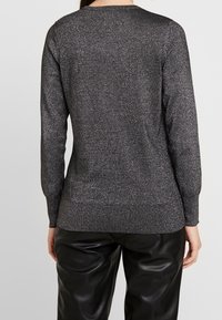 Svart glittrig tröja med långa ärmar, rund halsringning och ribbad fåll; har en texturerad, glänsande yta mot en ljus bakgrund.