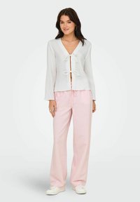 Haut blanc à manches longues et devant ouvert avec un détail de nœud à l'avant, assorti à un pantalon rose clair à jambes larges avec un motif rayé subtil.