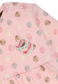 Helles rosa Kleidungsstück mit großen, pastellfarbenen Punkten und einem Einhorn-Patch. Weicher Stoff mit einem gerafften Volant am Saum.