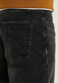 Svarta denimjeans med en distinkt design på bakfickan, subtila sömdetaljer och en liten logotyp på sidokanten.
