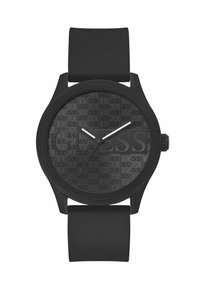 Sat s crnim silikonskim remenom s reljefnim crnim brojčanikom na kojem je urezana "GUESS" oznaka, bijelim kazaljkama za sate i minute, i okruglim kućištem.