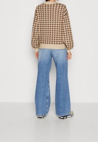Brun och beige houndstooth-tröja med ballongsärmar, ihop med ljusblå vida jeans. Mjuk textur; neutral färgpalett.