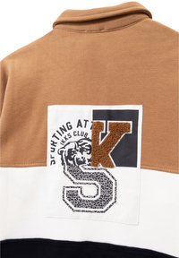 Bruin, wit en marineblauw color-blocked sweatshirt. Kenmerkend door een gestructureerde logo patch met een beerafbeelding en de letters "K" en "S." Zachte stof.