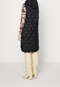 Černá prošívaná vesta s kapucí, která má diamantový vzor. V kombinaci s béžovými kozačkami po kolena, které se vyznačují jemnou strukturou.