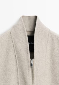 Hellgrauer Wollmischmantel mit hohem Kragen, Reißverschluss vorne und strukturierter Oberfläche, mit einem einfachen, minimalistischen Design.