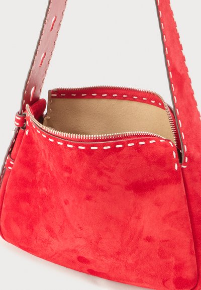 Κόκκινο σουέτ τσάντα ώμου με λευκές ραφές, ανοιχτό φερμουάρ και φαρδιά λουράκι που αποκαλύπτει τη σουέτ εσωτερική επένδυση.