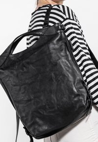 Schwarzer Leder-Rucksack mit glatter Oberfläche, ausgestattet mit einem verstellbaren Riemen und einem Tragegriff. Einfaches Design ohne sichtbare Beschläge oder Muster.