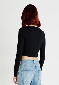 Zwarte, langemouw cropped top met een ronde hals, gecombineerd met lichtblauwe high-waisted jeans met een vervaagde textuur en achterzakken.
