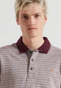 Korte mouwen polo shirt in maroon met licht gestreept patroon, voorzien van een maroon kraag en een drieknopenlijst met geborduurd logo.