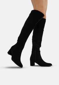 Botas negras de ante hasta la rodilla con tac�ón de bloque y detalle de cremallera en el lateral. La textura suave y el diseño ajustado realzan la elongación de las piernas.