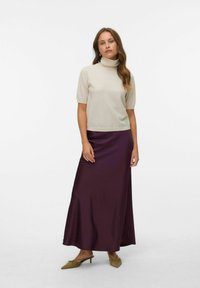 Beige t-shirt met kol en korte mouwen, gecombineerd met een lange, vloeiende paarse satijnen rok. Het model draagt olijfgroene schoenen met een spitse neus.