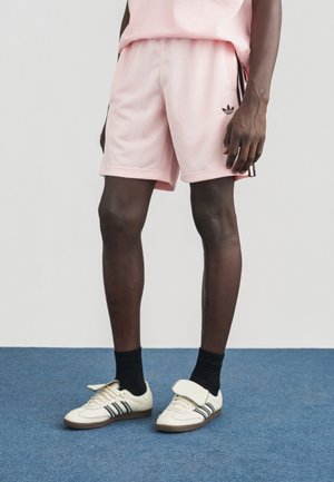 Svetloružové športové šortky s bočnými pruhmi, v kombinácii s béžovými teniskami so čiernymi a bielymi detailmi a textúrovanými akcentmi.