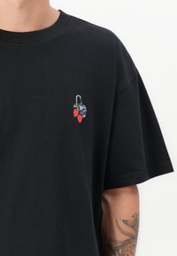 Sort oversized t-shirt med et lille broderet design af kirsebær og et kranium, lavet af blødt bomuldsstof med rund halsudskæring.