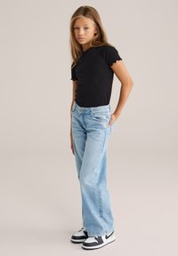 Czarna, prążkowana koszulka z falbankowymi rękawami, jasnoniebieskie szerokie jeansy oraz czarno-białe trampki. Prosty design bez widocznych wzorów.