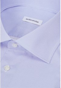 Gros plan d'une chemise habillée violet clair avec un petit motif hexagonal et des boutons blancs, étiquetée "seidensticker" sur l'étiquette du col.