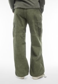 Pantaloni cargo verde oliva realizzati in tessuto morbido, con gambe larghe, tasche laterali e un dettaglio con cordoncino all'orlo.